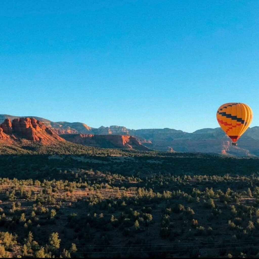 hot air balloon floating in blue sky across a red rock desert landscape