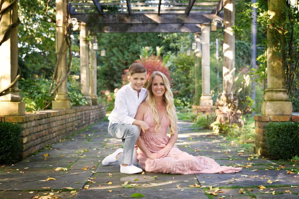 mother and son sitting on a cobblestone road under a garden archway