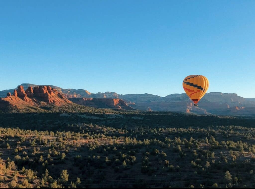 hot air balloon floating in blue sky across a red rock desert landscape