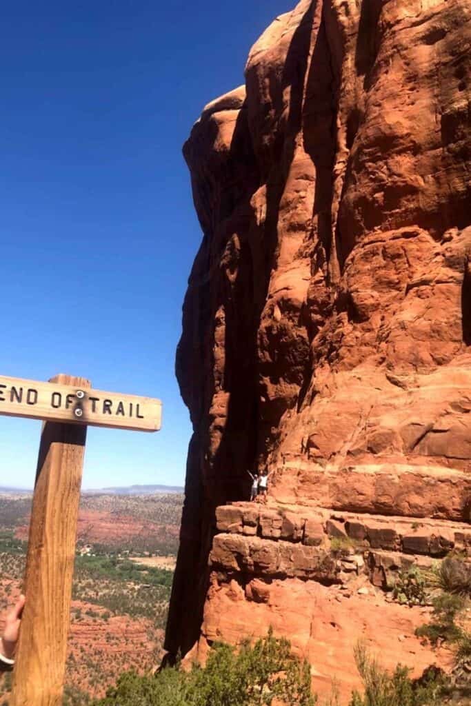 wooden sign that says end of trail with mother and son standing in the background on an edge of a red rock cliff mountain top 