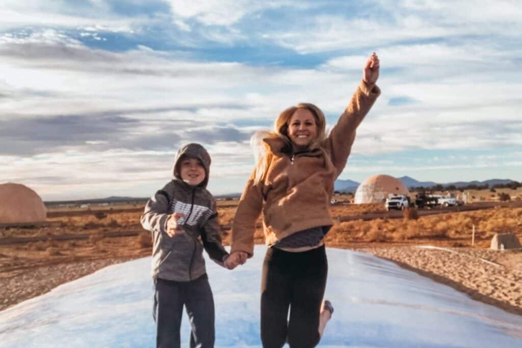 mother and son jumping on a blue trampoline bag in the middle of a desert