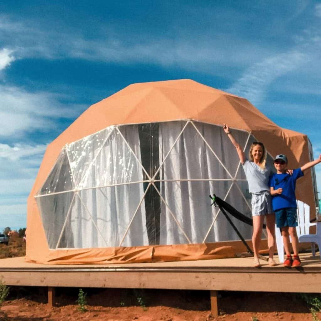 mother and son standing in front of a tan tent dome with blue sky in background
