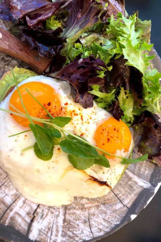 a plate of medium hard eggs on top of avocado toast and arugula salad on the side