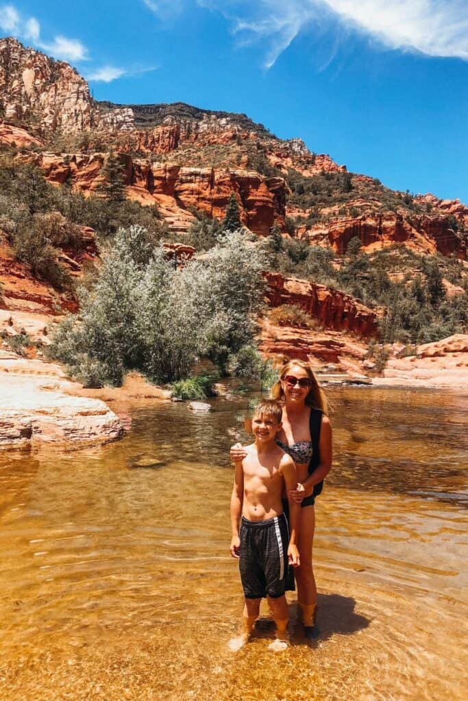 mom and son in bathing suits standing in a river with a red rock mountain landscape at Slide Rock state park 