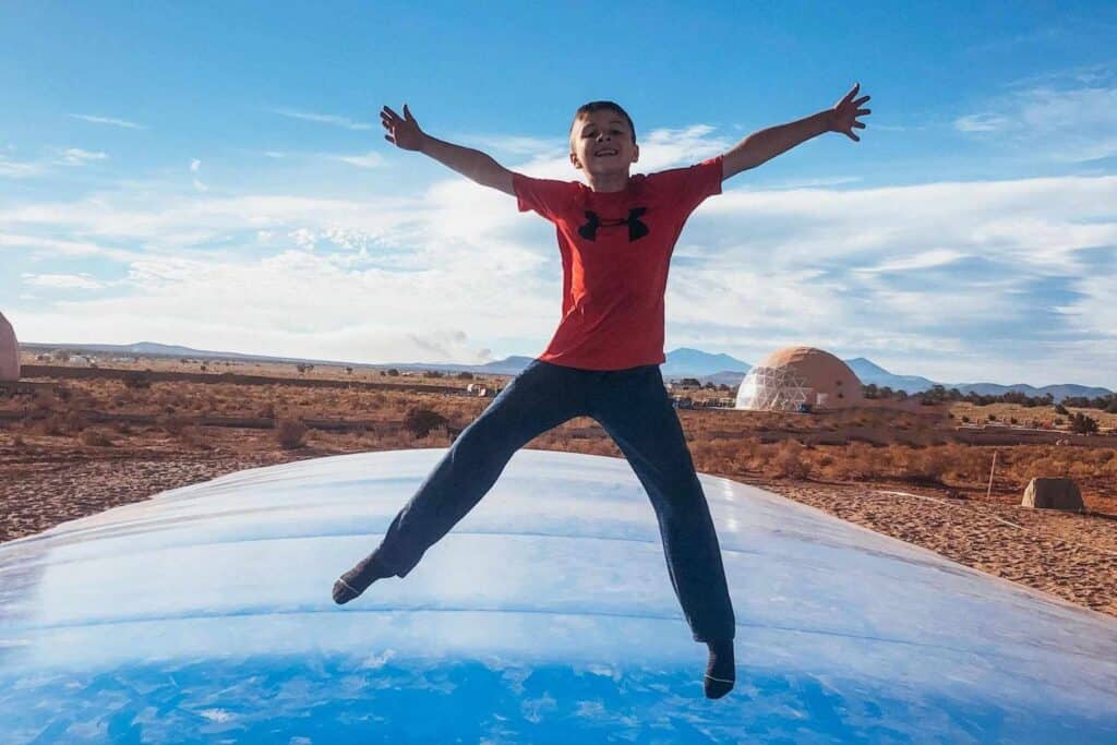 boy in a red shirt jumping on a blue inflatable bounce trampoline in the middle of the desert with a mountain range in the background at Clear Sky Resorts Grand Canyon 
