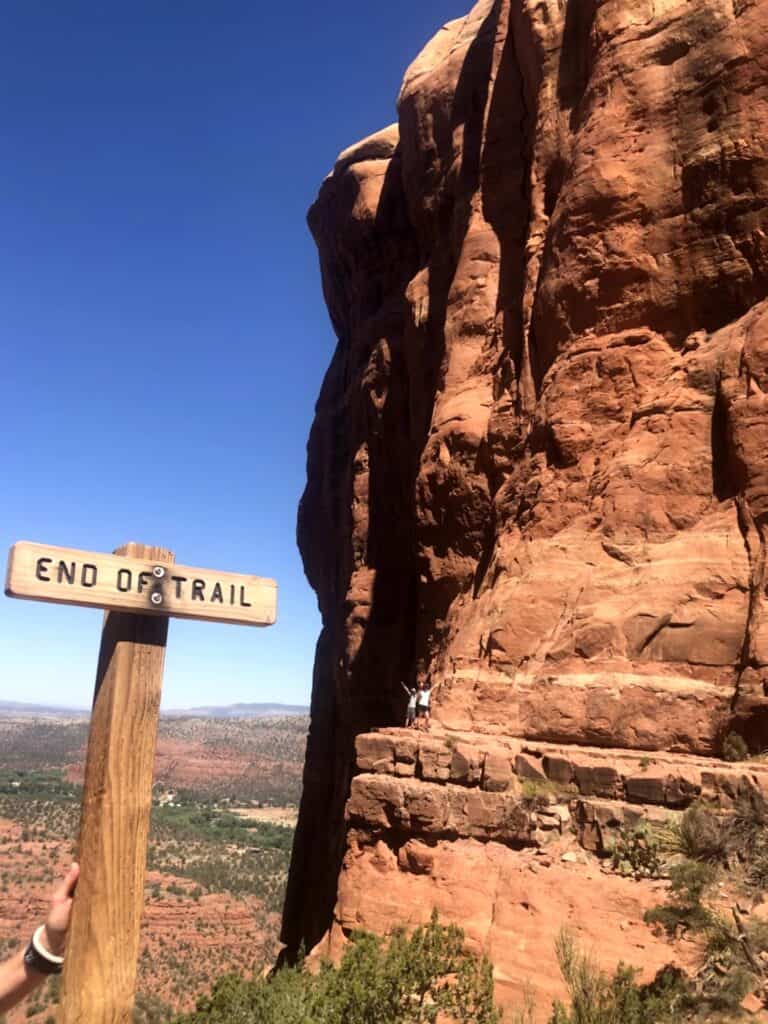 Hiker standing in the back of End of Trail sign at Cathedral Rock in Sedona, Arizona with red rock cliffs in the background
