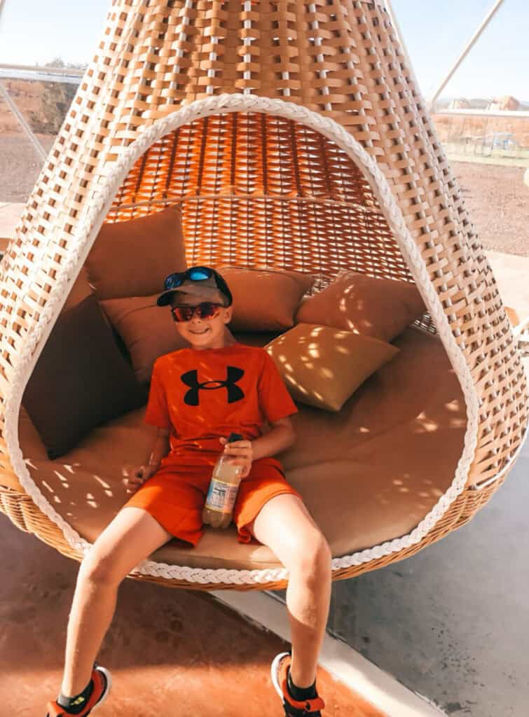 boy in a red shirt and shorts swinging in an enclosed wicker swing