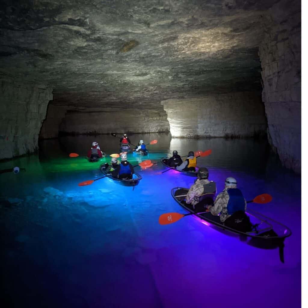 glow in the dark kayaks reflecting different colors in water in a dark cave