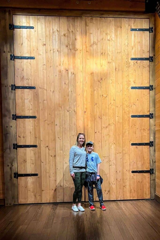 mom and son standing in front of a big wooden door with a light reflection of a cross on the door