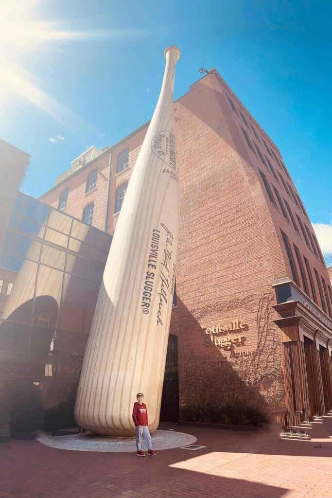 giant bat with boy in red sweatshirt in front of red brick building with blue sky