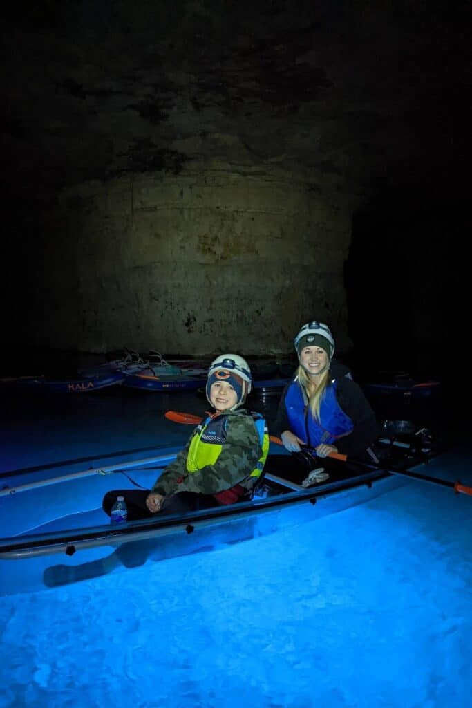Mother and son sitting in a glow in the dark kayak reflecting blue on the water in a dark cave