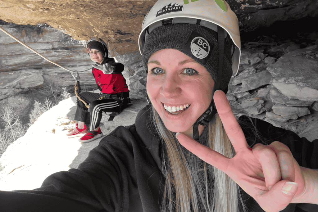 mom and son in a cave wearing white helmets smiling giving the peace sign with their hands