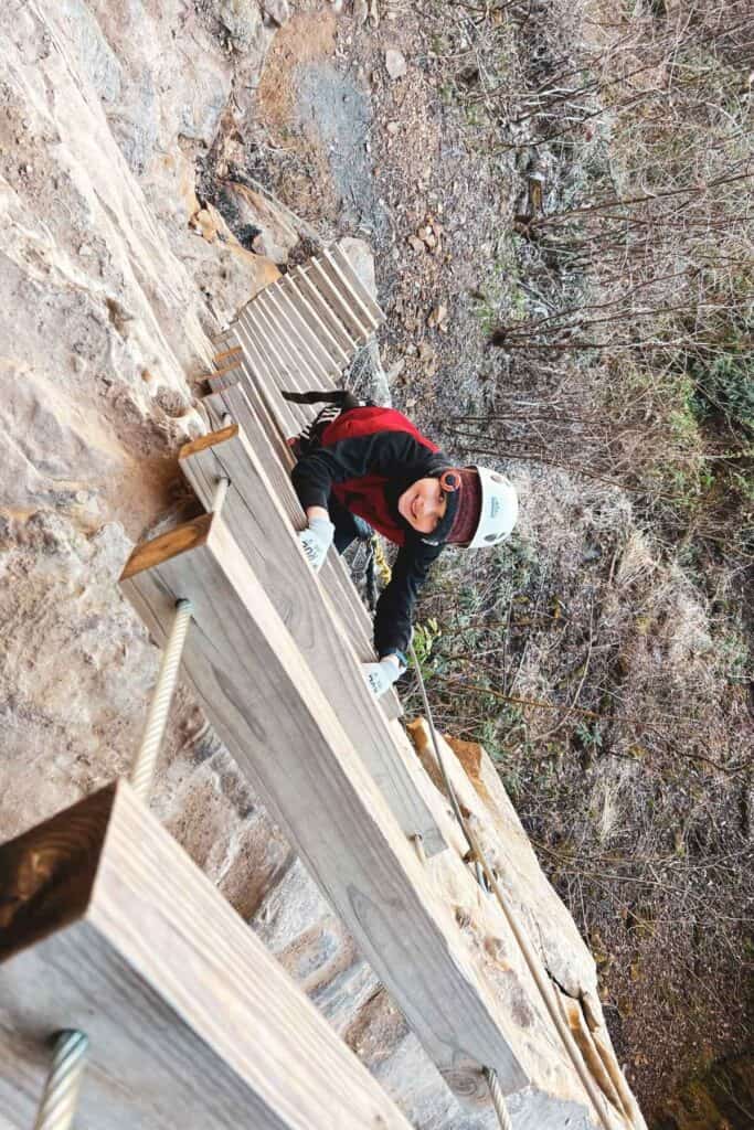 boy descending a wooden latter on the side of a cliff