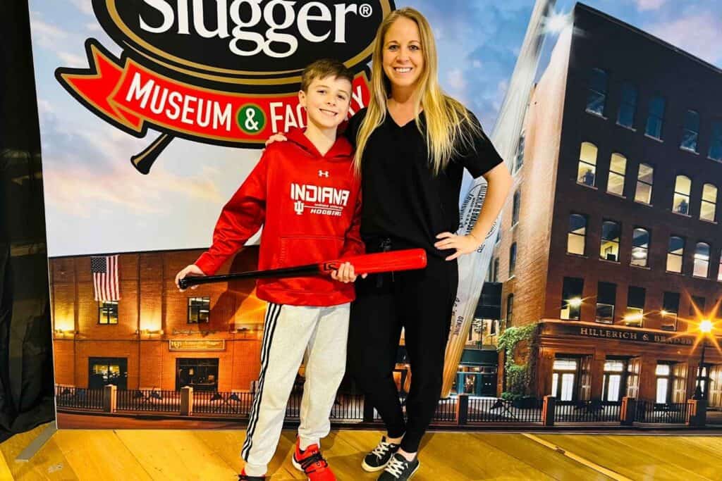 mother wearing a black outfit and son wearing a read sweatshirt smiling with a red and black baseball bat