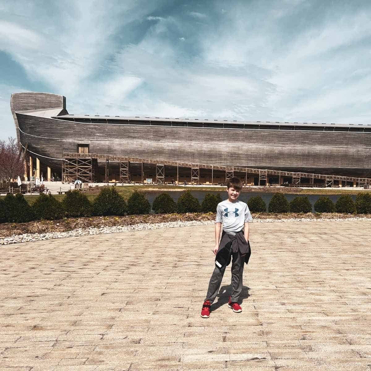 a boy standing on a tan brick road in front of a big wooden boat