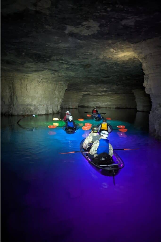 flood mining cavern with 6 kayaks glowing in a variety of colors with people paddling