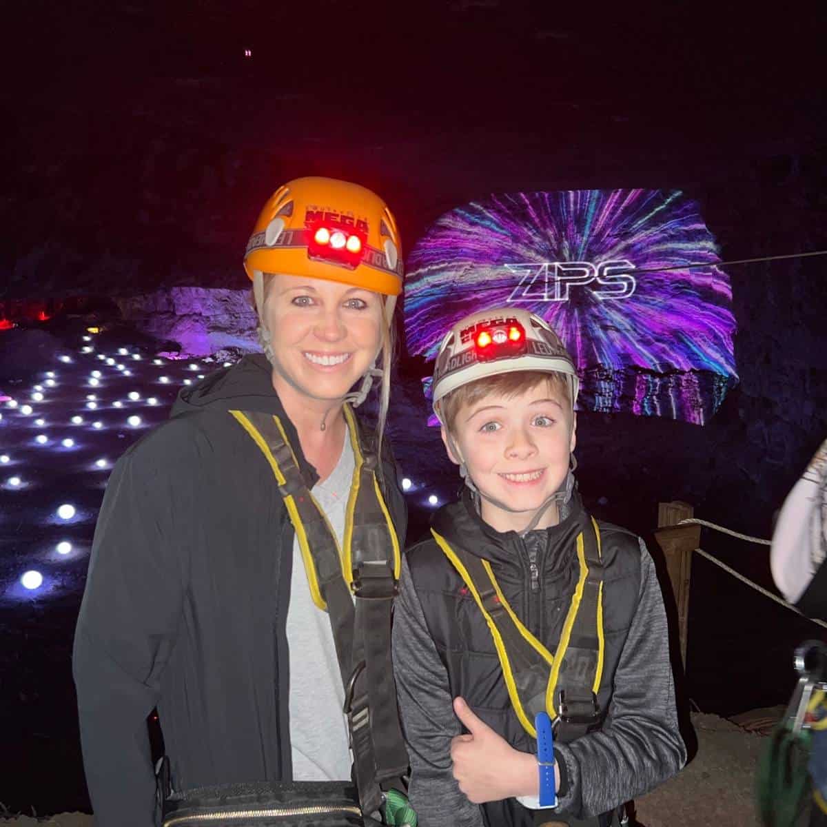 mom and son wearing ziplining gear with a laser light show in background