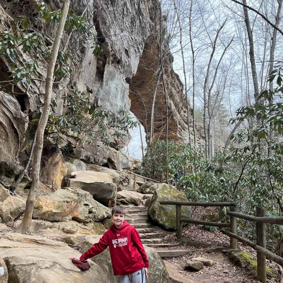 boy in red sweatshirts standing in front of a natural rock bridge
