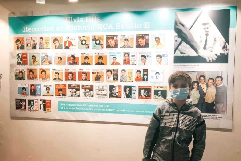 Boy in grey jacket standing in front of a wall at RCA Studio B, surrounded by iconic photographs showcasing Elvis Presley's hit songs recorded at the legendary studio 