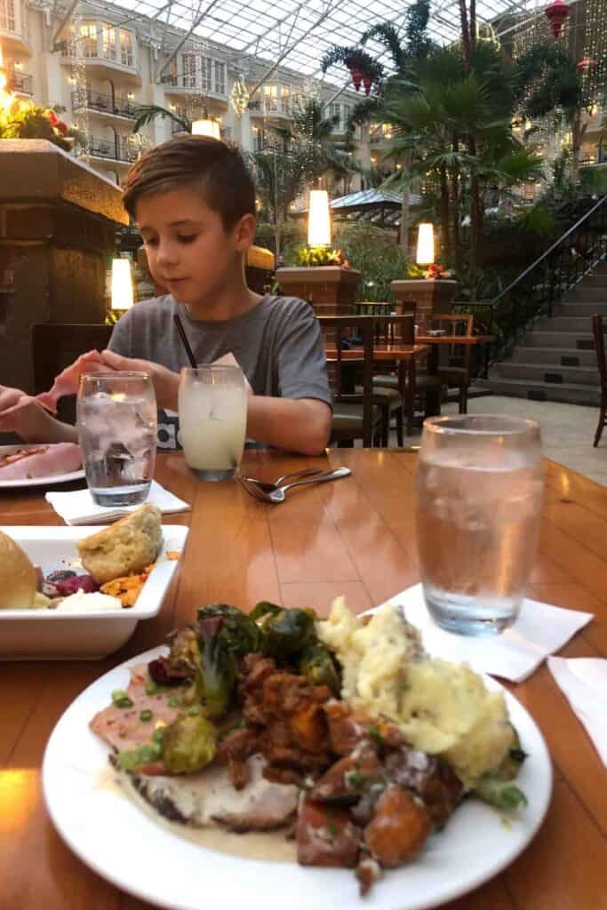 boy in grey shirt eating mashed potatoes, beef and broccoli at a brown table with a glass of water at Gaylord Opryland Resort