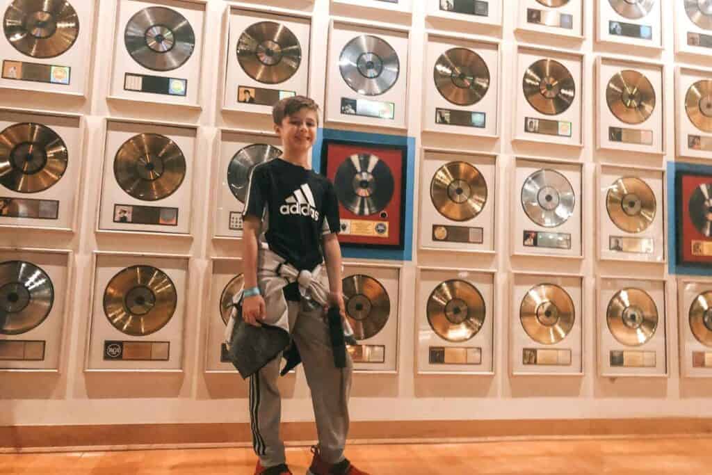 boy in black shirt and grey sweatpants standing in front of a wall filled with records at the Country Hall of Fame