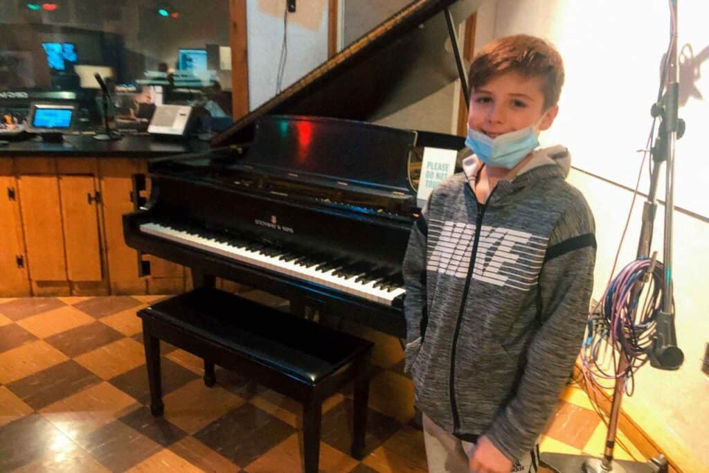 Boy in a grey shirt standing in front of the famous black grand piano at RCA Studio B, a key in instrument in many iconic Elvis Presley recordings