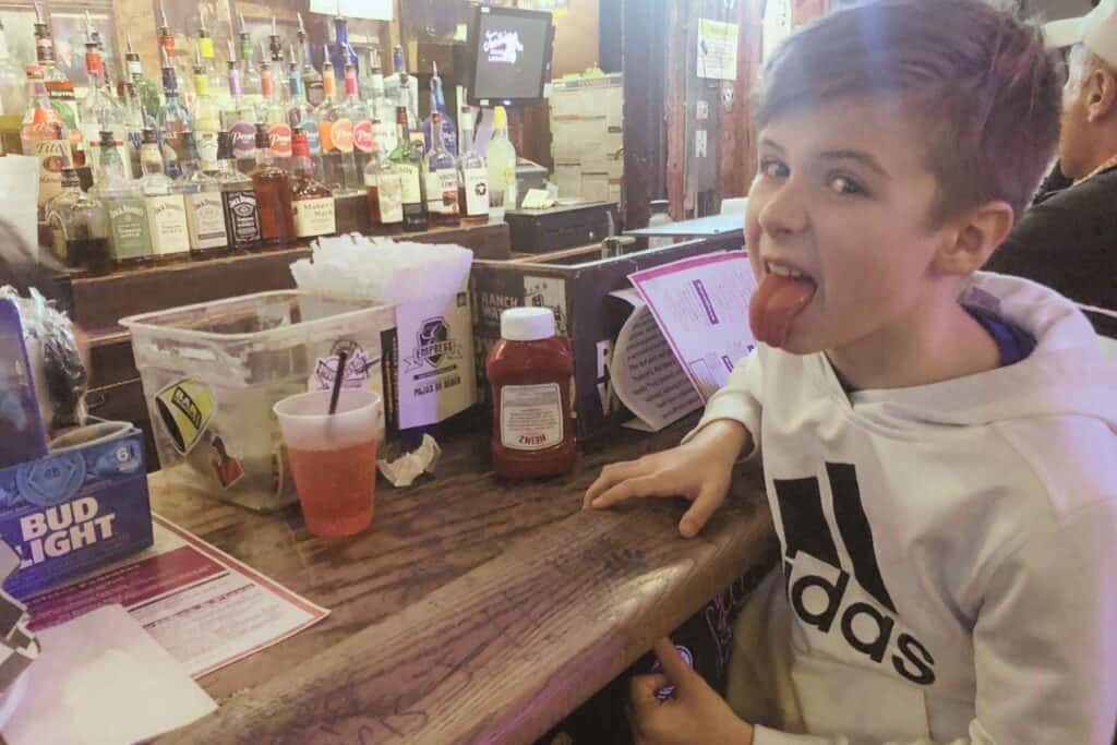 boy in white sweatshirt sitting at a bar drinking a kiddie cocktail at Tootsies Orchid Lounge