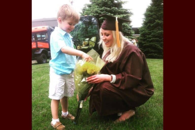 Mother in graduation cap kneeling beside her young son as he gives her flowers, capturing a heartfelt moment of love and connection