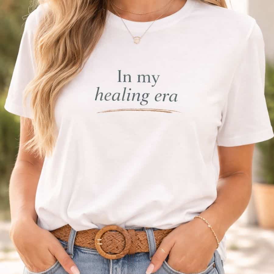 White graphic t-shirt with the phrase In my healing era printed on the front in soft sage and taupe lettering